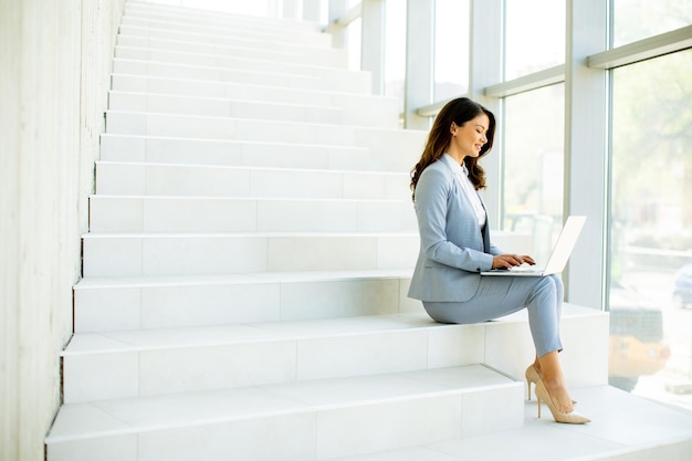 Young business woman sitting on the stairs on office hallway and working on laptop