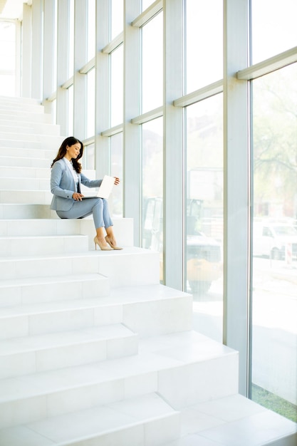 Young business woman sitting on the stairs on office hallway and working on laptop