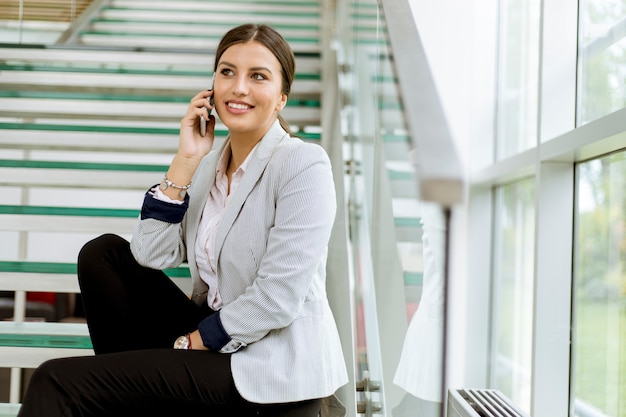 Young business woman sitting on the stairs at the office and use mobile phone