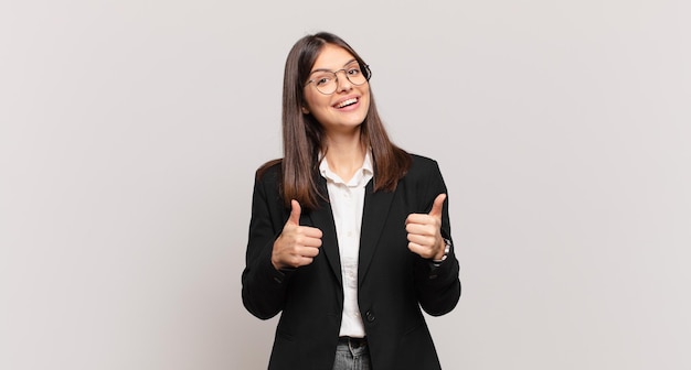 Young business woman smiling broadly looking happy positive confident and successful with both thumbs up