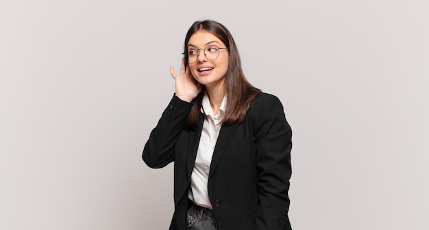 Young business woman smiling, looking curiously to the side, trying to listen to gossip or overhearing a secret