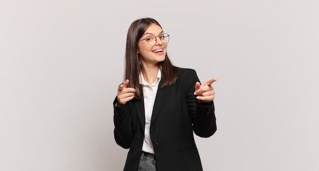 Young business woman smiling with a positive, successful, happy attitude pointing to the camera, making gun sign with hands