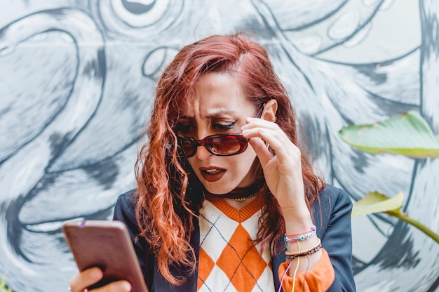 Young business woman squinting and confused looking at her mobile screen with concern