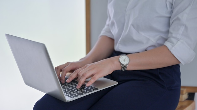 A young business woman uses a laptop placed on her leg in the office.