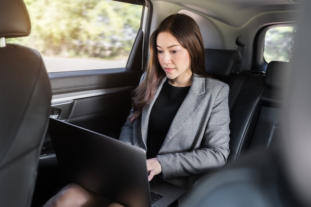 Young business woman using laptop computer while sitting in the back seat of car