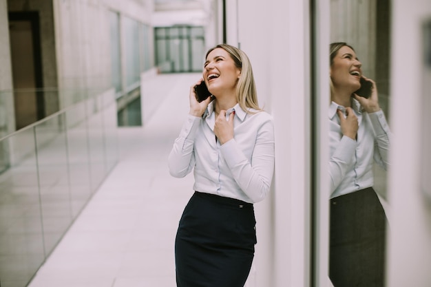 Young business woman using mobile phone in the office hallway