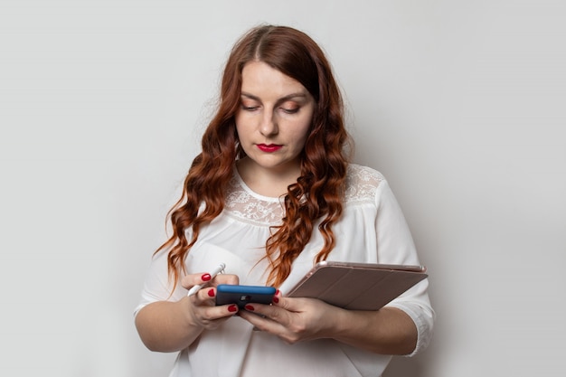 Young business woman with a beautiful curly hairstyle is using a smartphone and holding a tablet. Projects and work . Confident business expert.