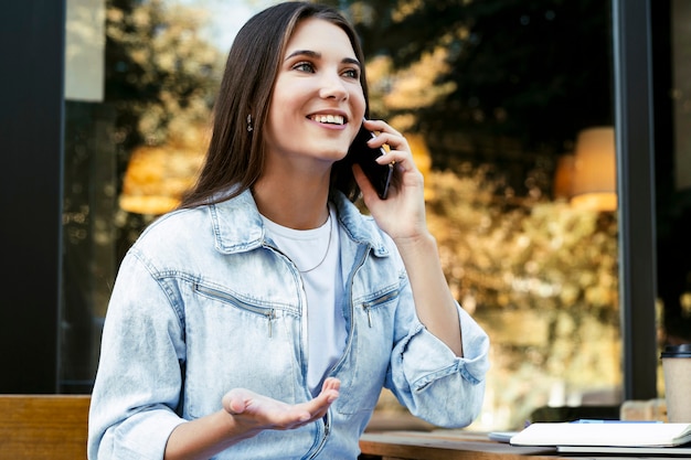 Young business woman working in cafe on open terrace, sitting in front of laptop, talking on the phone.