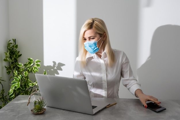 Young business woman working from home, wearing protective mask.