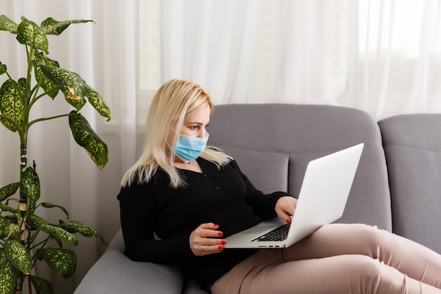 Young business woman working from home with laptop, wearing protective mask