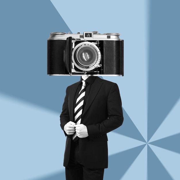 A young businessman in a black business suit headed by huge old vintage retro photo camera