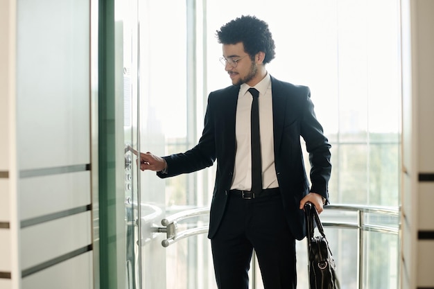 Young businessman in black suit with briefcase using elevator in modern office building