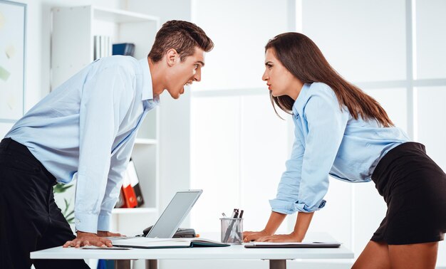 Young businessman and businesswoman staring at each other with hostile expressions. They are have a conflict on a work.