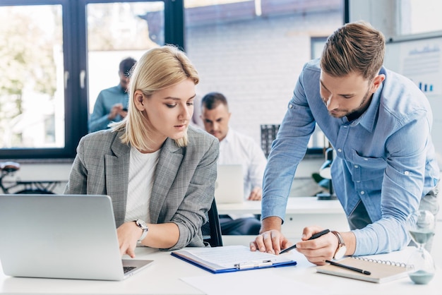 Young businessman and businesswoman working with papers and laptop in office