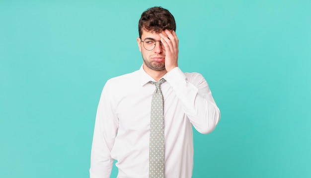 Young businessman feeling bored, frustrated and sleepy after a tiresome, dull and tedious task, holding face with hand