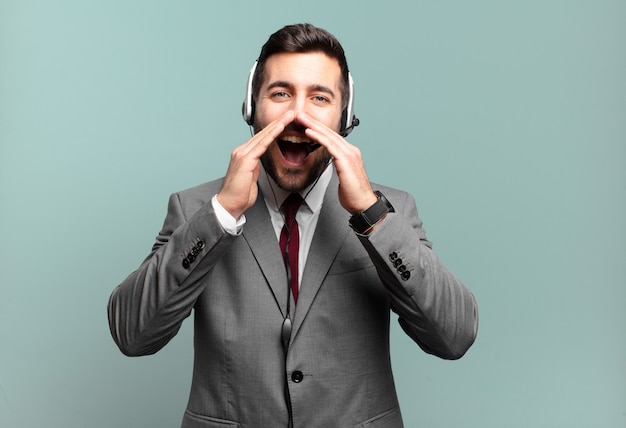 Young businessman feeling happy, excited and positive, giving a big shout out with hands next to mouth, calling out telemarketing concept