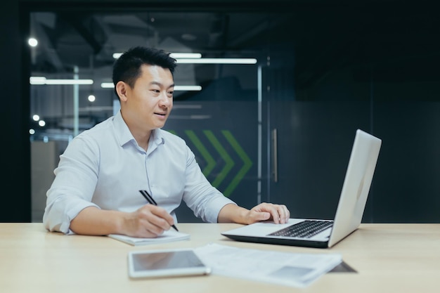 Young businessman freelancer asian working with documents writing with a pen working on a laptop