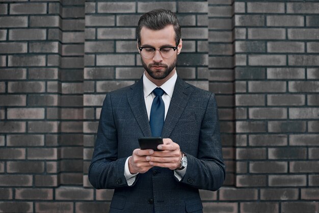 A young businessman in glasses and an expensive suit works on a smarphone in his