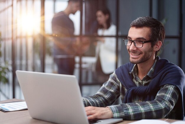 Young businessman in glasses works with a computer remotely sitting at the table