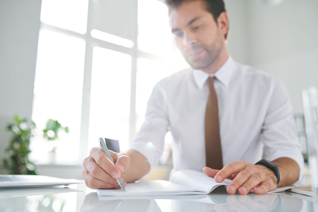 Young businessman making notes while planning his working day by desk in office