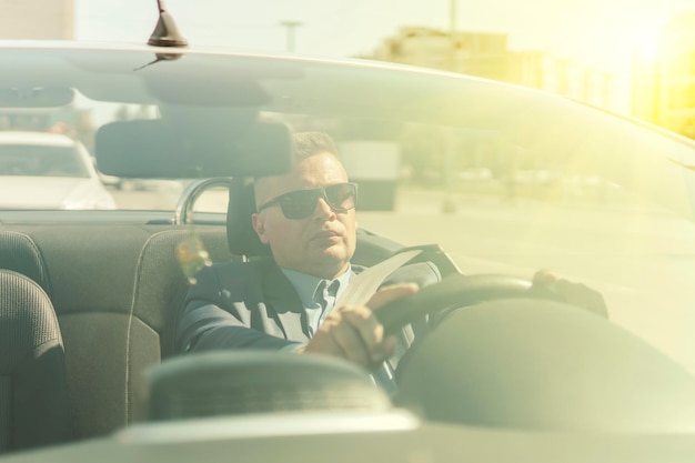 Young businessman rides in a convertible car in the summer with a satisfied expression on his face