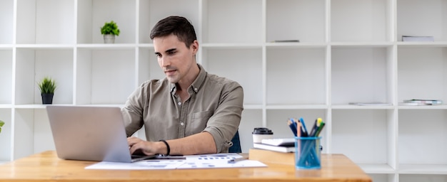 Young businessman sitting in the office with a laptop, typing messages with partners through chat, he founded a startup, he is a young businessman who is skilled in running a growing company.