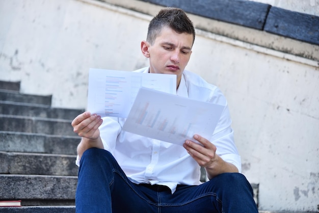 Young businessman sitting on stairst and analyzes financial data