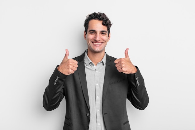 Young businessman smiling broadly looking happy, positive, confident and successful, with both thumbs up