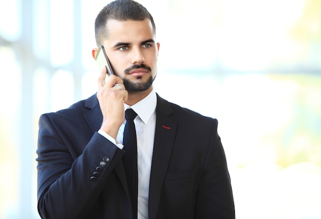 Young businessman standing in office lobby, using smartphone, smiling.