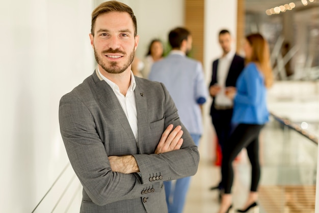 Young businessman standing in the office and other young business people talking in the background