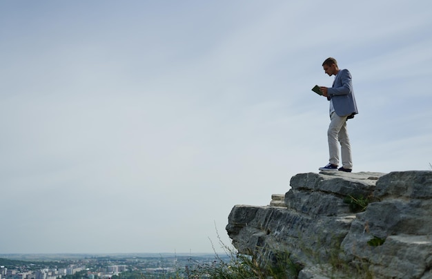 Young businessman stands on a rock and looks at his tablet