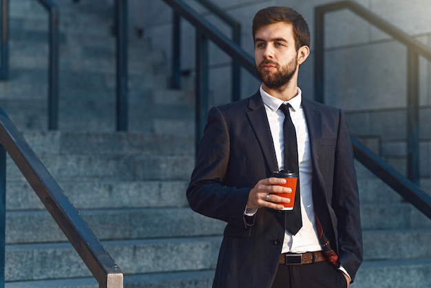 Young businessman in a suit  holding a red paper cup of coffee look to the side.