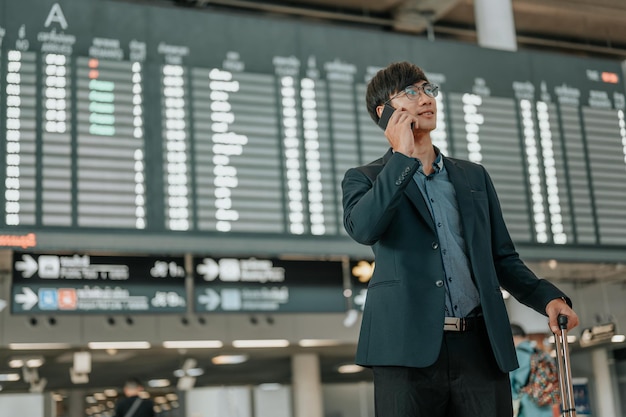 Young businessman at timetable screen board using smart phone.Flight board.