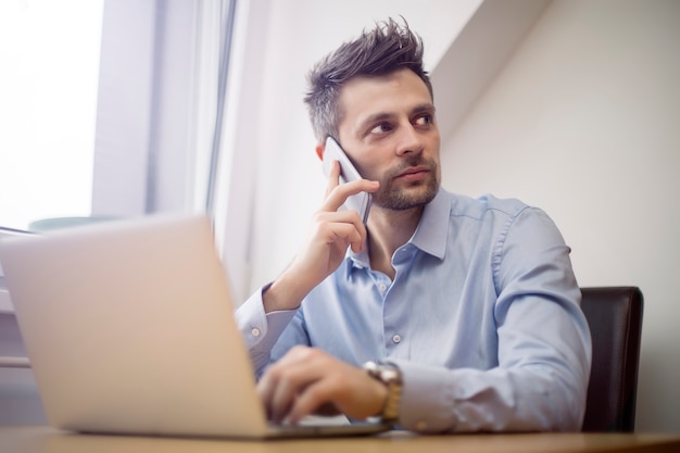 Young businessman using mobile phone and working on laptop