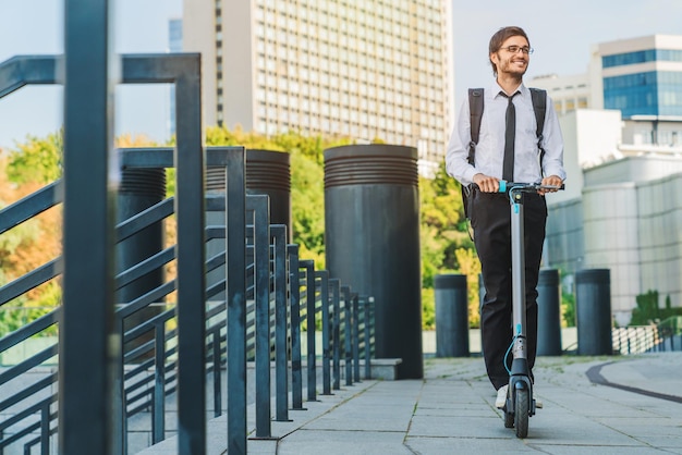 Young businessman with backpack on his back riding on scooter to work at city street