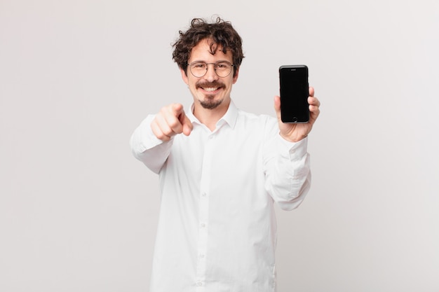 Young businessman with a cell pointing at camera choosing you