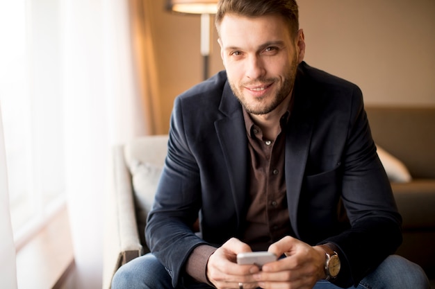 Young businessman with mobile phone by window