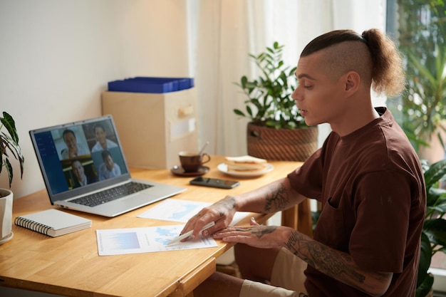 Young businessman working at his home office checking report and having online meeting with colleagues