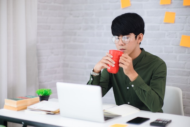 Young businessman working at home and drinking coffee. He look at laptop. Soft and smooth focus and tone