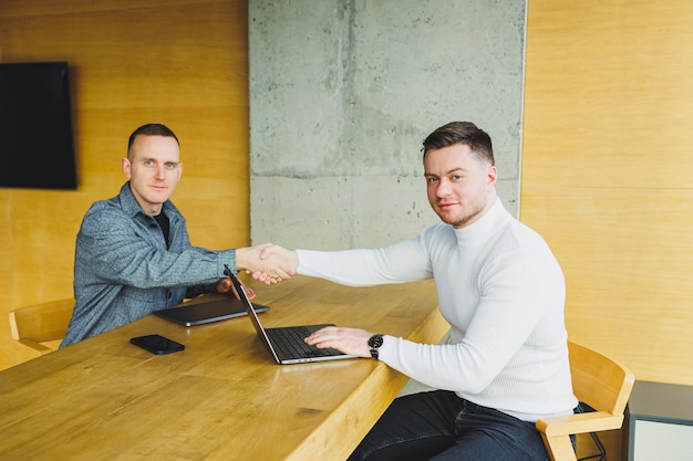 Young businessmen two male colleagues while working with a laptop in the office Two businessmen collaborate in a modern workspace Two young businessmen work in a bright office