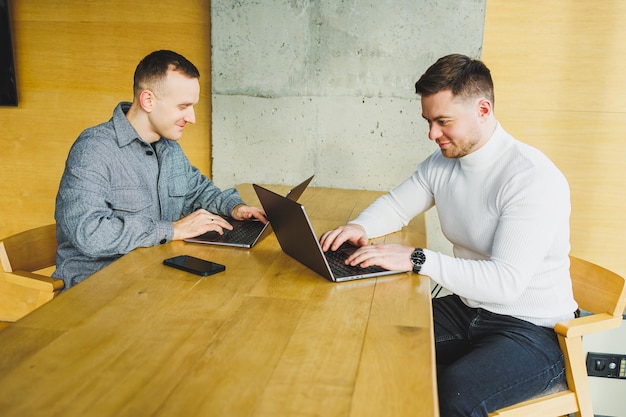 Young businessmen two male colleagues while working with a laptop in the office Two businessmen collaborate in a modern workspace Two young businessmen work in a bright office