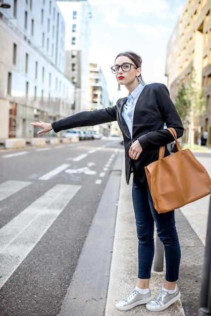 Young businesswoman catching a taxi standing on the street at the modern residential district