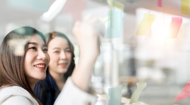 Young businesswoman creative team using post it notes in glass wall to writing strategy business plan to development grow to success