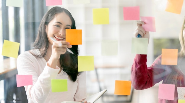 Young businesswoman creative team using post it notes in glass wall to writing strategy business plan to development grow to successx9