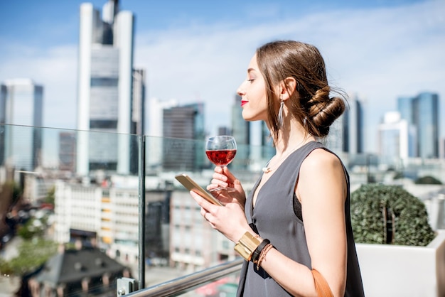 Young businesswoman enjoying wine on the terrace with great view on the skyscrapers in Frankfurt city