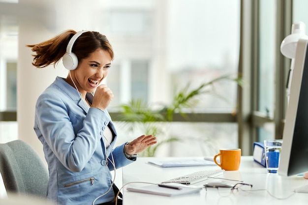 Young businesswoman having fun and signing while listening music over headphones in the office