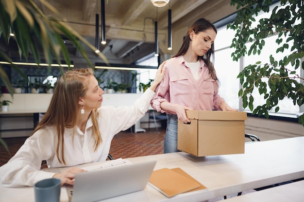 Young businesswoman holding box of personal belongings about to leave office after quitting job