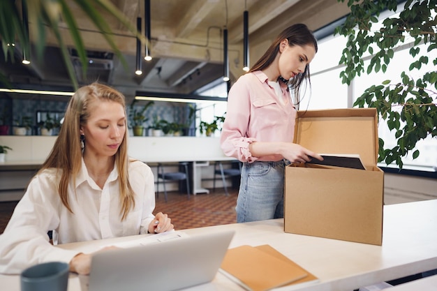 Young businesswoman holding box of personal belongings about to leave office after quitting job