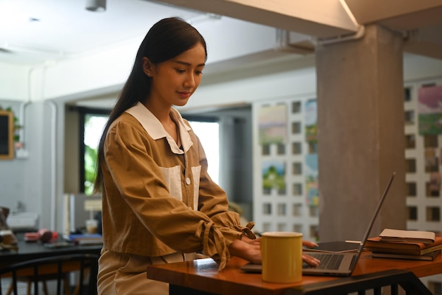 Young businesswoman sitting in contemporary coffee shop and using laptop computer