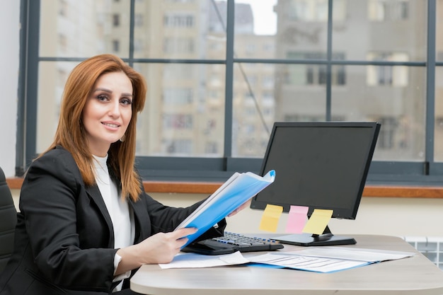 Young businesswoman sitting at the desk and holding her notebook